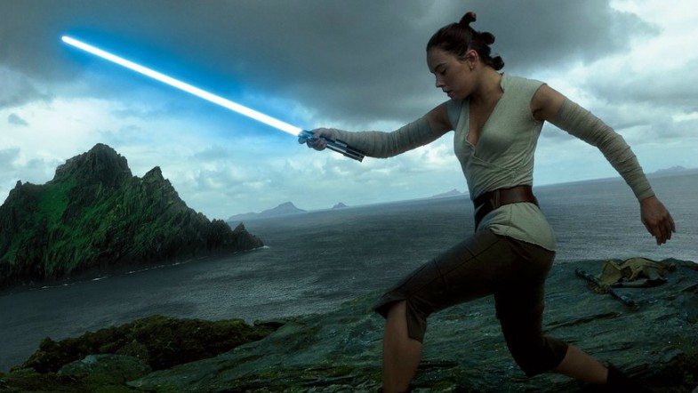 Rey holds a blue lightsaber against a dark, stormy ocean backdrop.