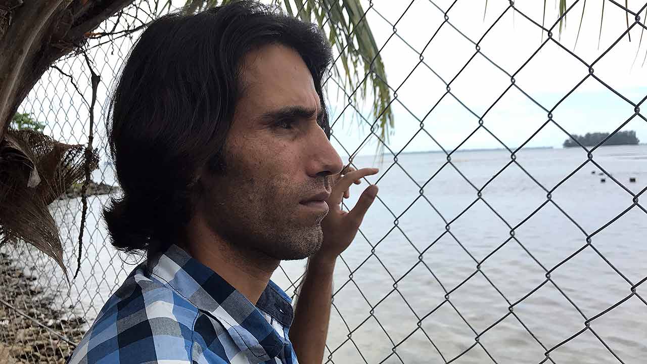 Boochani looks out through a fence towards the open ocean