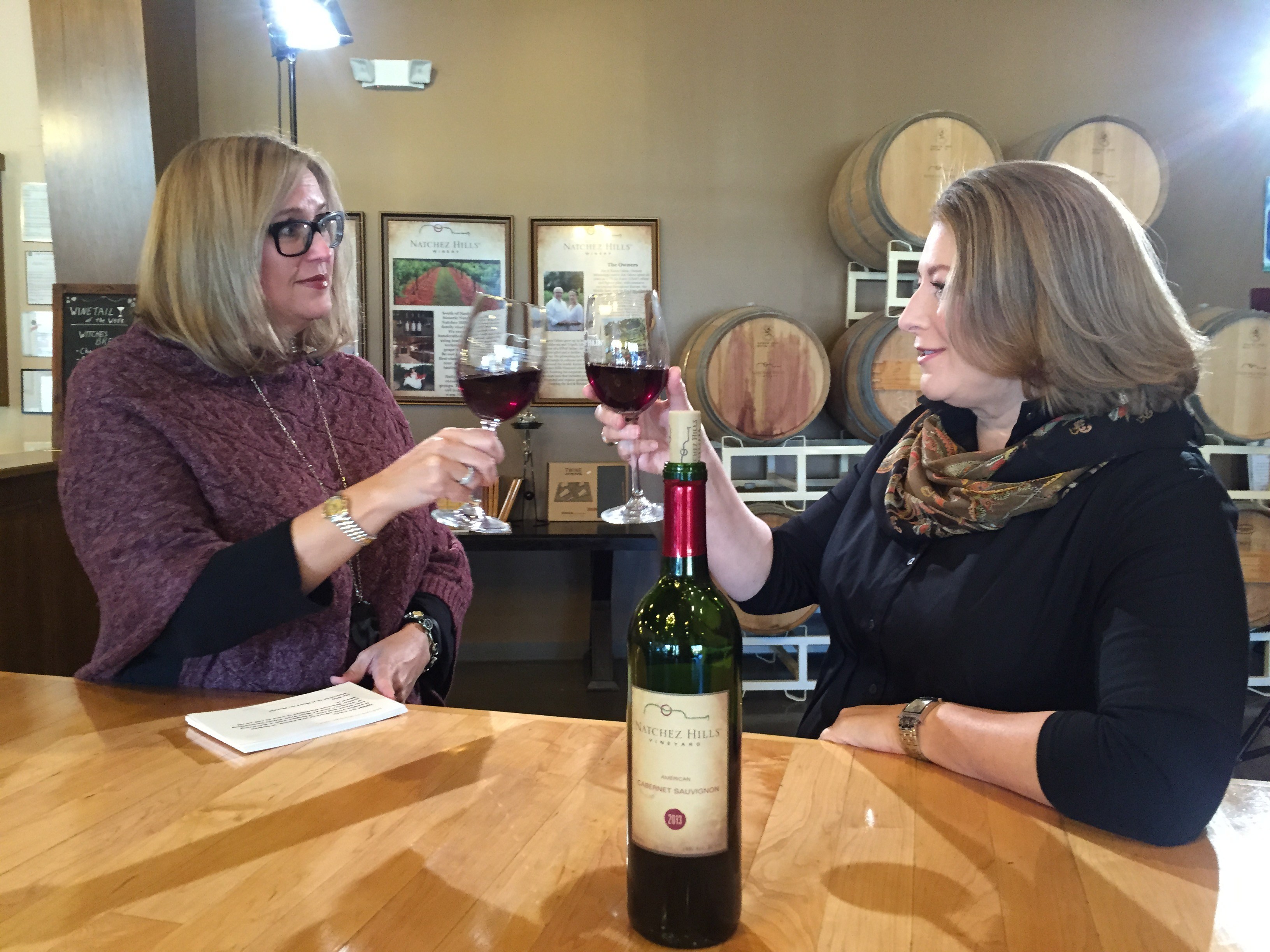 Harkness and a friend cheers glasses of red wine with red wine bottle in foreground on table 
