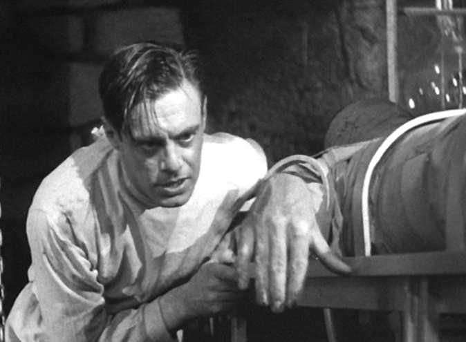 Victor Frankenstein leans over the inert form of the monster in his lab