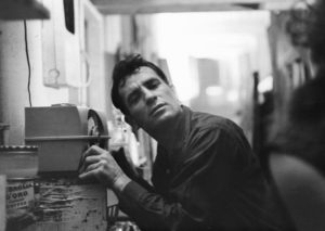 Jack Kerouac sitting at a stove, facing the camera in a black and white portrait