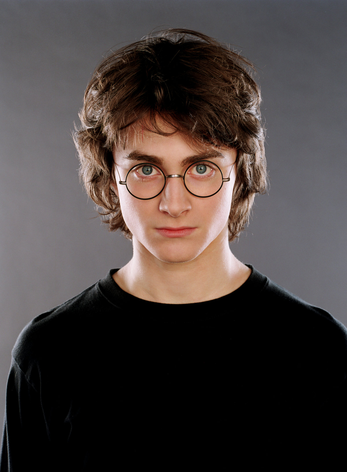 Harry Potter stands in front of a blank background, glasses on