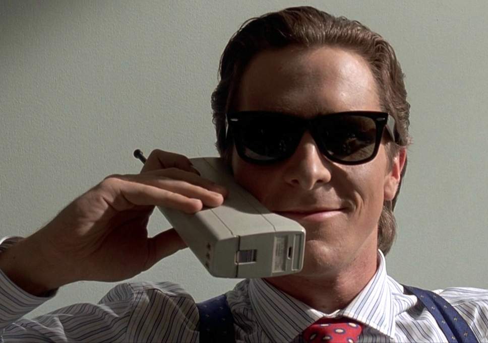 Christian Bale as Patrick Bateman sits in a business suit on a cell phone