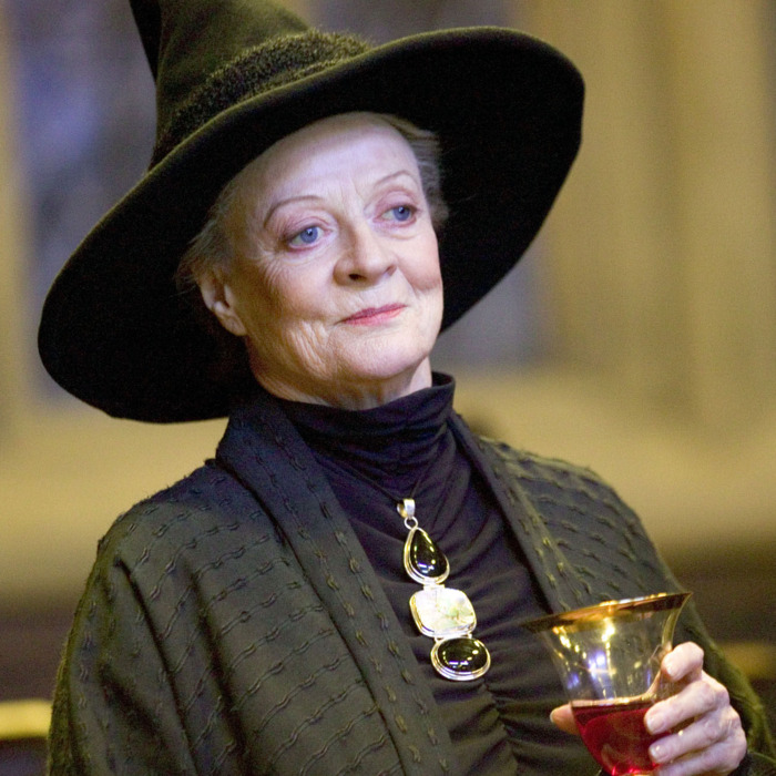 An elderly lady wearing a witch's hat and holding a glass of wine.