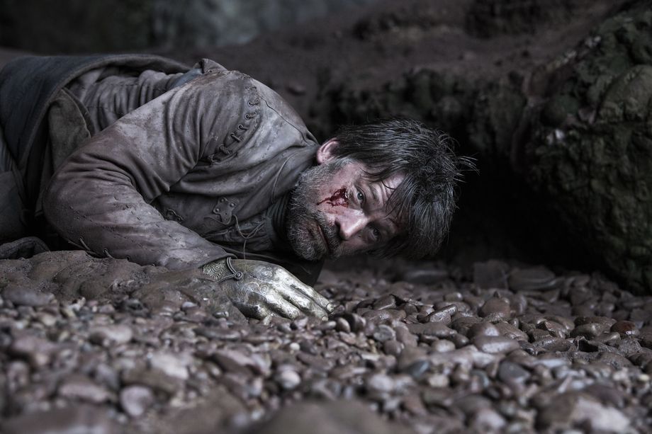 Jamie Lannister lies wounded on a rocky beach, faced covered with dust and blood