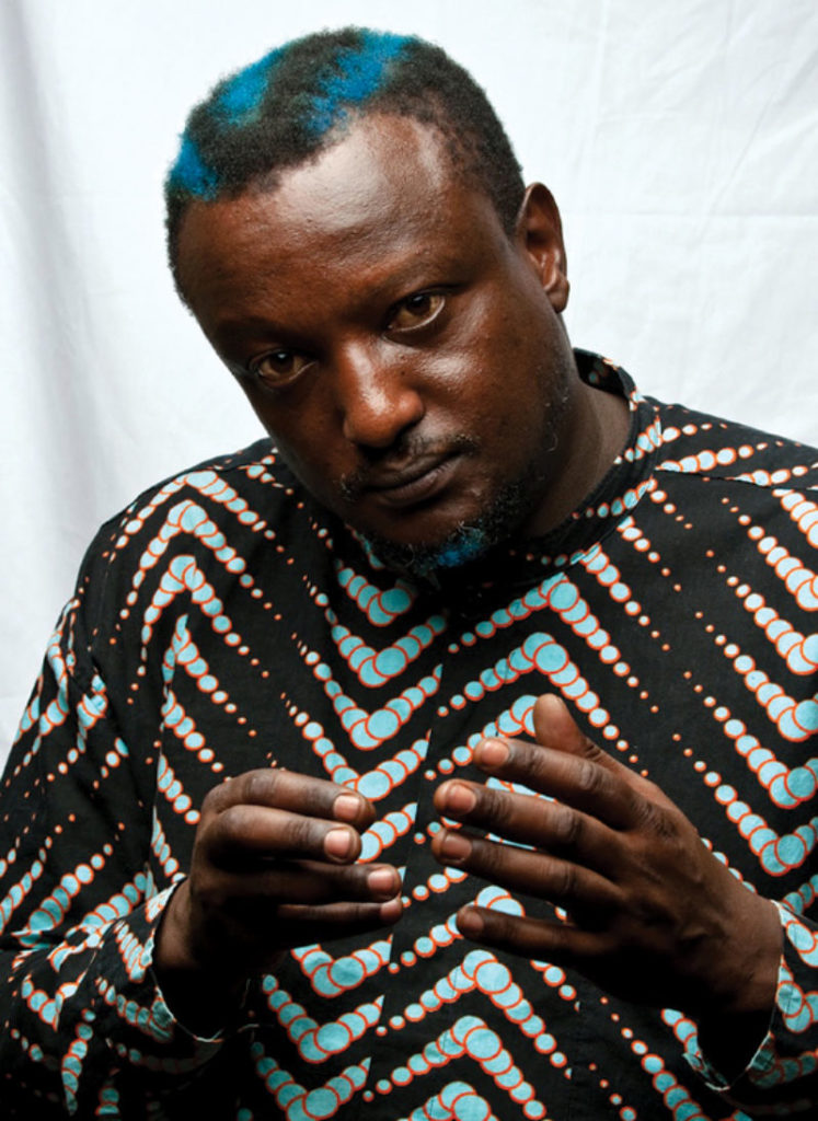 Kenyan writer Wainaina stares at the camera, parts of his hair dyed blue 