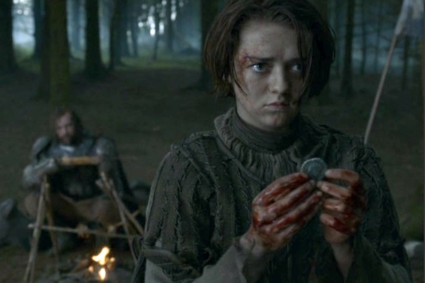 Arya stands with a coin in hand as Sander Clegane lounges in the background around a campfire