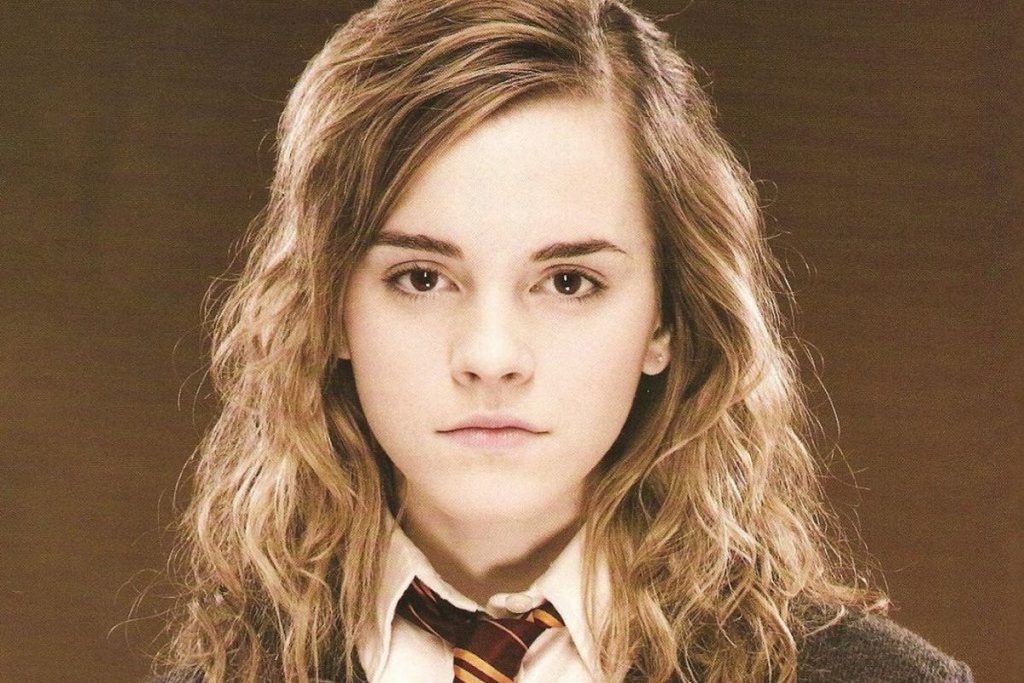 Hermione stands in her school uniform against a brown backdrop