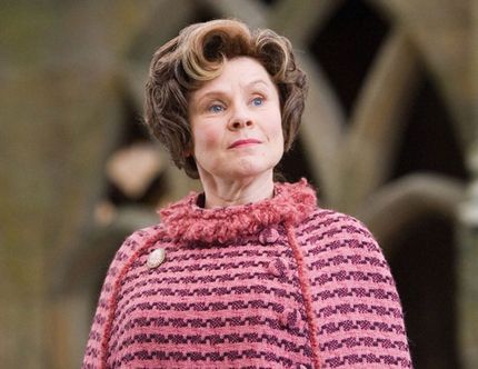 Dolores Umbridge, a middle aged woman dressed in a pink sweater stands at attention