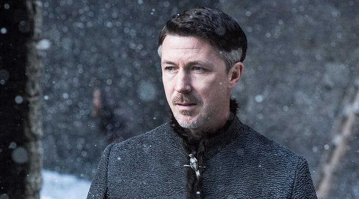 A man stands in a snowy field wearing a grey tunic 