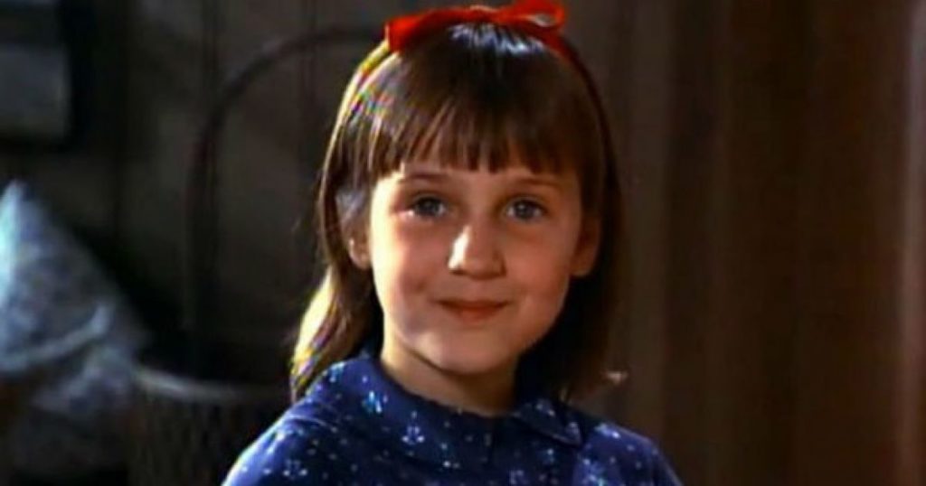 Matilda stands on a bed with a crafty smirk