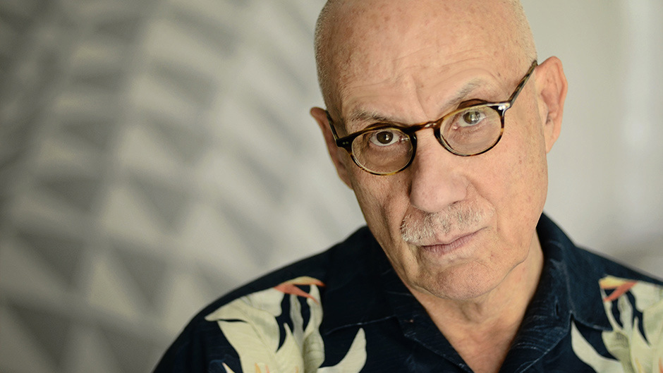 A close up portrait of writer James Ellroy, framed against a white backdrop