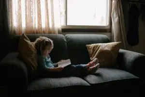 Little girl reading small book on green couch