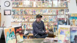 An older man sitting in front of a wall of comic books