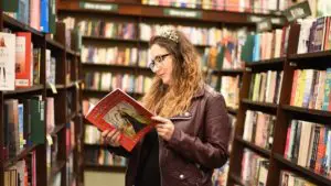 Image of a woman standing in a bookstore reading a book