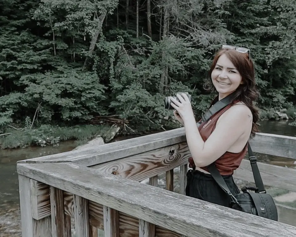 Image of woman holding a camera while standing on a porch with trees in the background