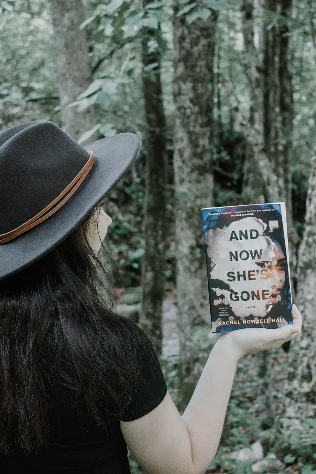 Image of a women standin in a forest balancing a book on her hand to show the cover
