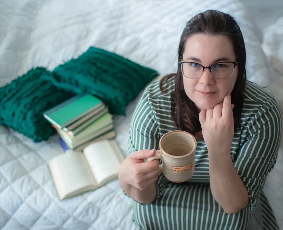 Woman holding a mug of coffee sittign next to an open book
