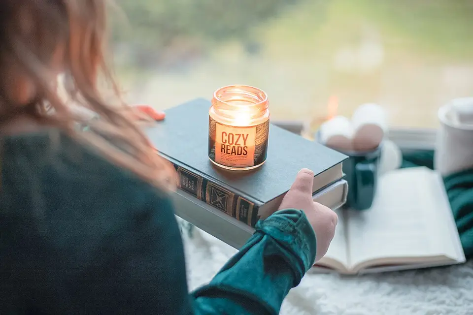 Image of a woman holding two books balancing a lit candle on top