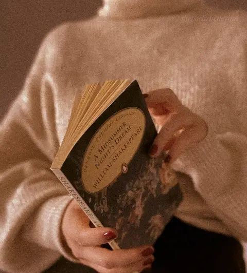 Image of a woman in a sweater holding A Midsummer Night's Dream