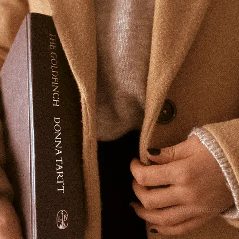 Close up image of a woman wearign a coat holding a book under her arm