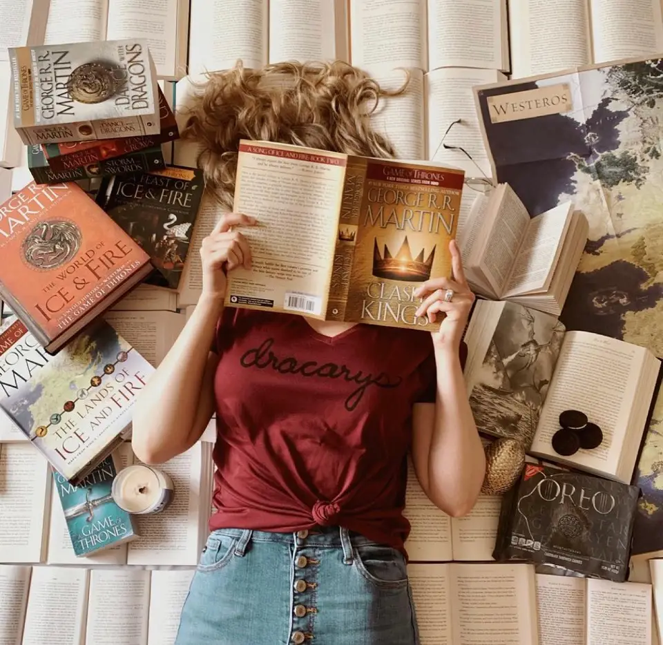 Image of a woman with a book in front of her face laying on her back surrounded by more books