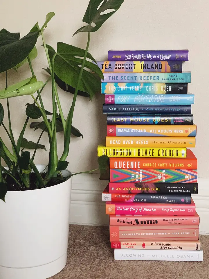 A stack of colorful books next to a plant in a white vase